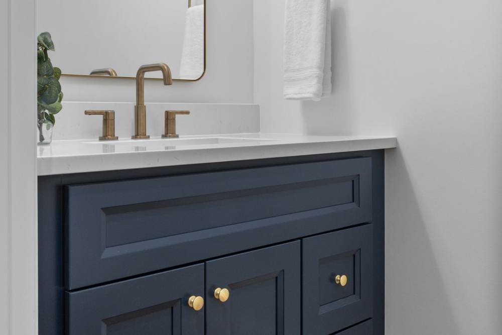 Navy blue bathroom vanity with a white quartz top, brushed brass faucet and pulls, under a sloped ceiling