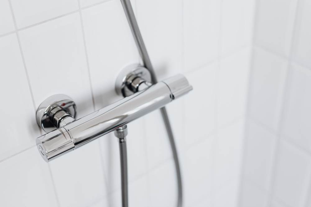 Chrome thermostatic shower mixer bar with a hand shower hose on white square tile