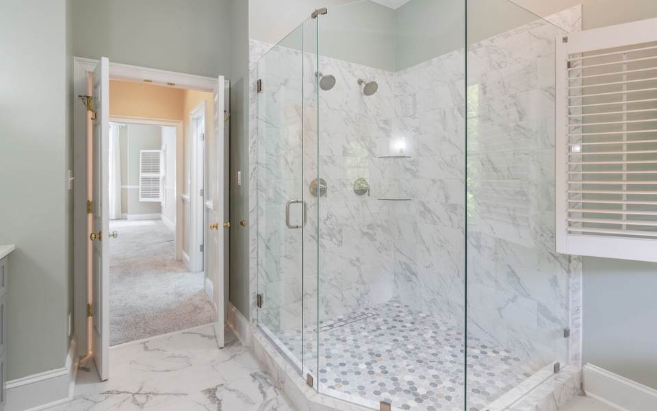 Marble-look tiled walk-in shower with two shower heads, a hex mosaic floor, a linear drain and frameless glass