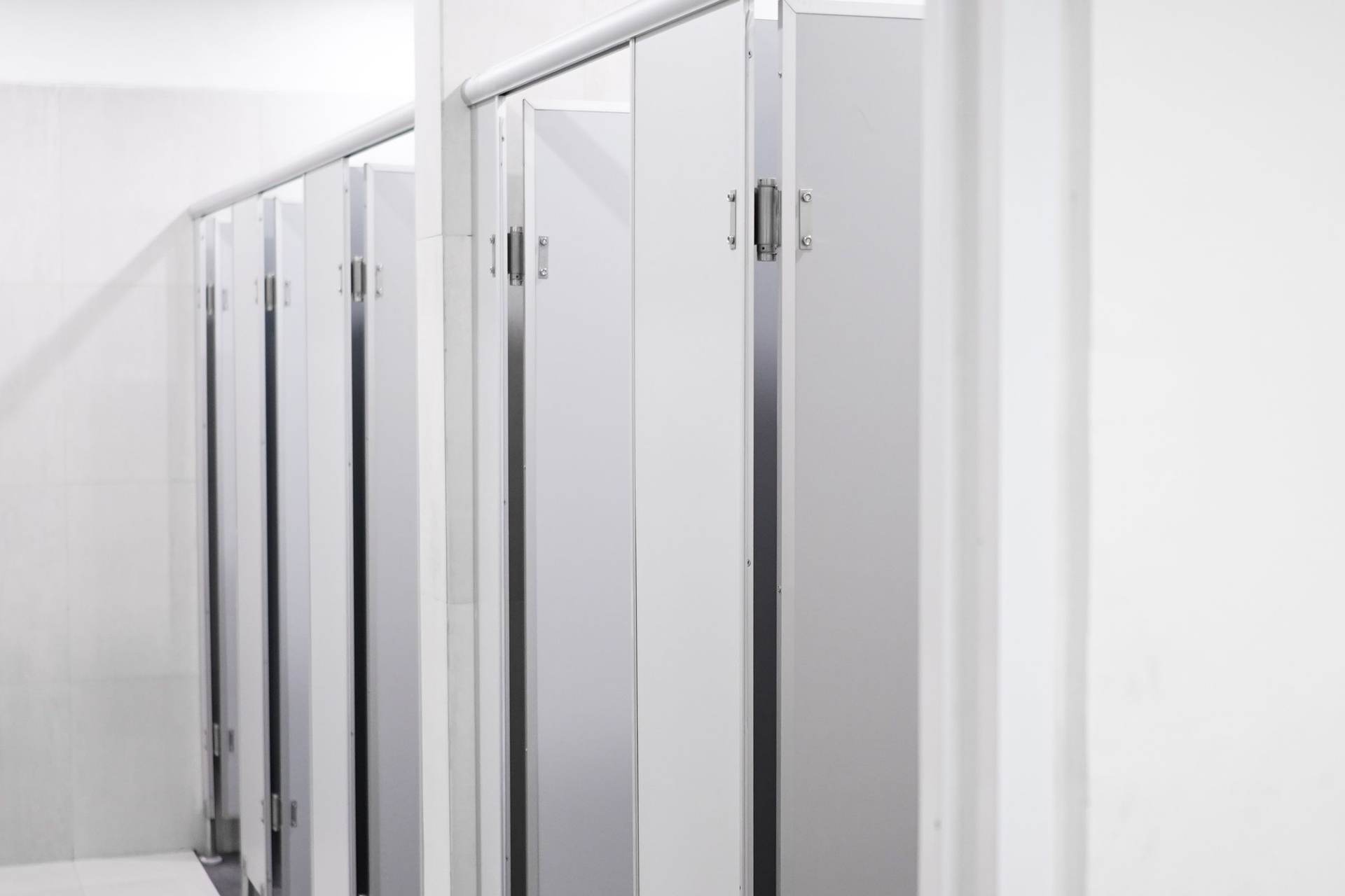 Row of white laminate toilet partitions with stainless hardware in a bright commercial restroom