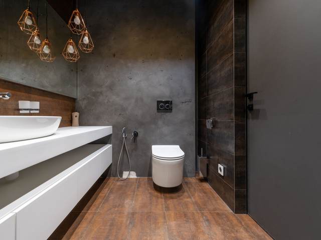 Modern bathroom with a wall-hung toilet against a concrete-look wall and a long white vanity