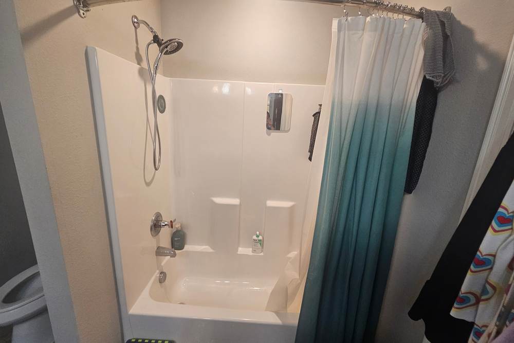 Molded fiberglass tub and shower combo with built-in soap shelves and a curtain, before we replaced it in a Bixby home