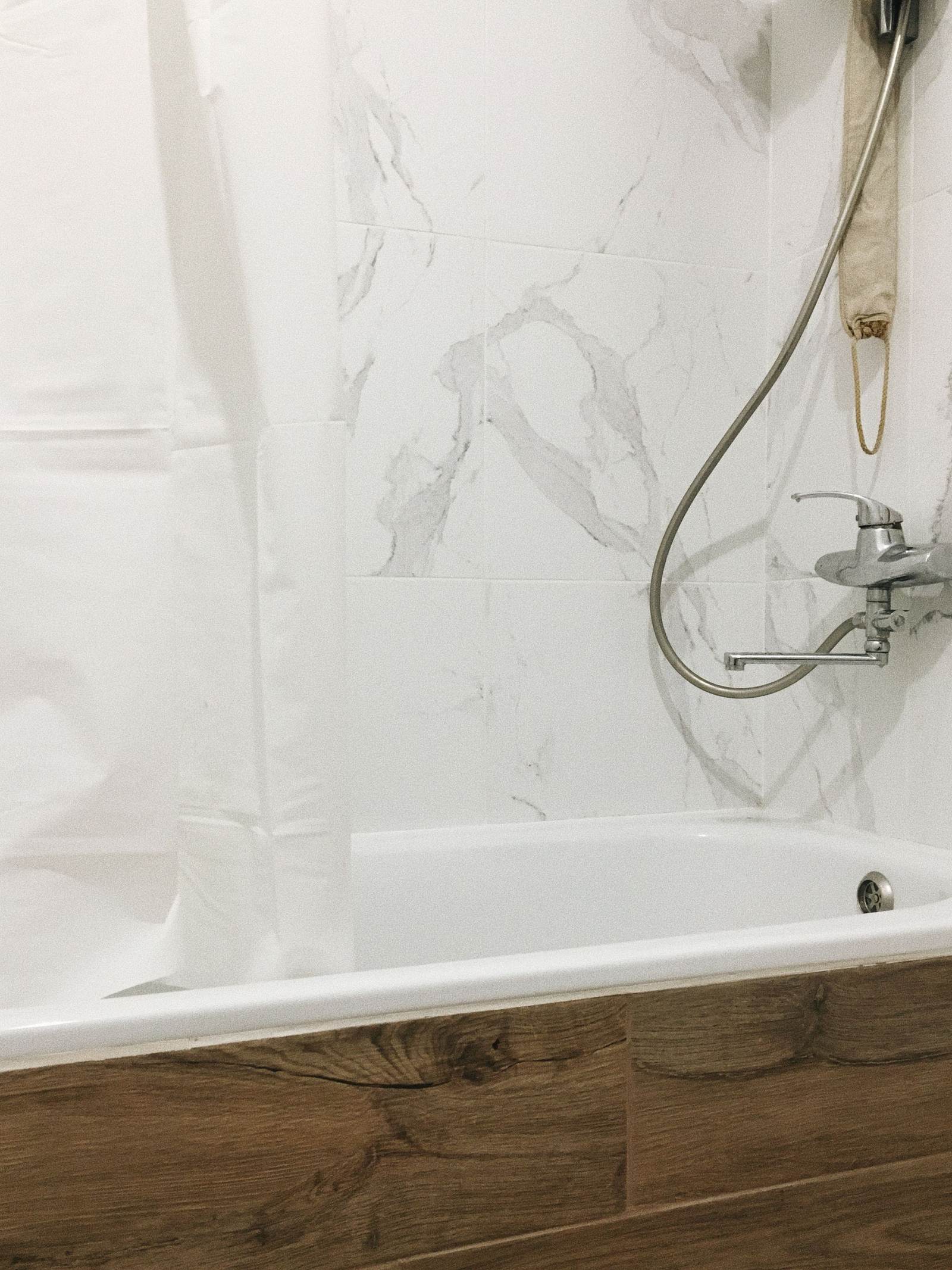 New white tub with marble-look wall tile and a wood-look tile apron below it