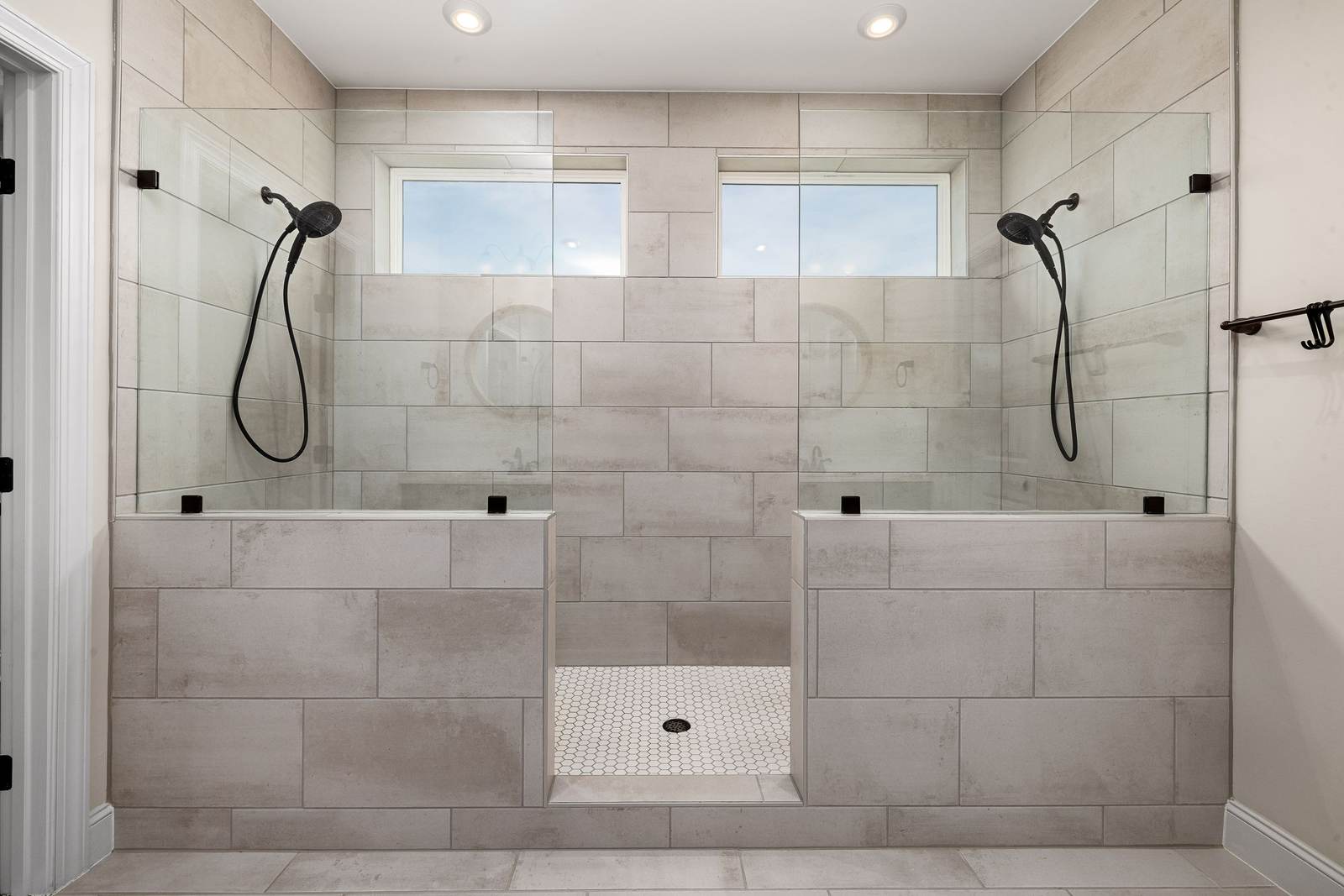 Wide tiled walk-in shower with two hand showers and half walls with glass panels, built where a tub used to be