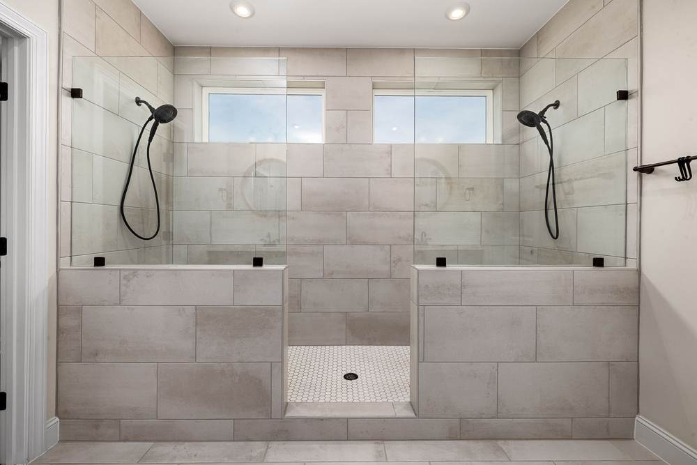 Double walk-in shower with a hand shower at each end, a tiled half wall and glass above it, under two windows