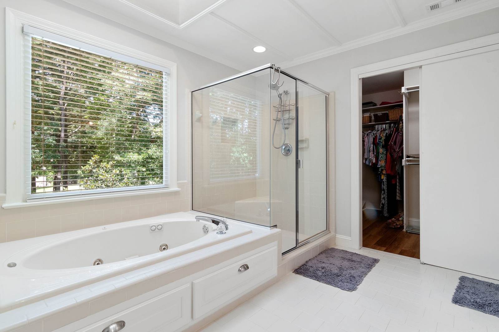 Primary bath with a white jetted tub on a deck beside a framed glass shower stall, the layout many 1980s and 1990s homes still have
