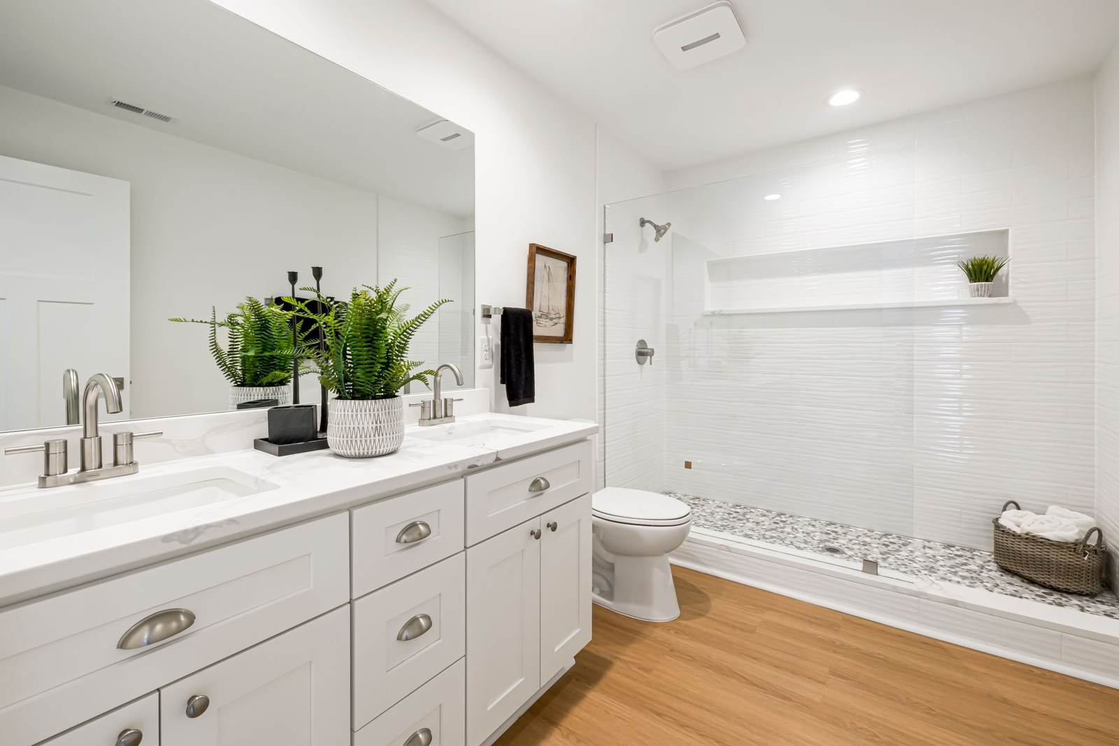 Long tiled walk-in shower with a frameless glass panel, a full-width niche and a pebble mosaic floor, beside a white shaker vanity
