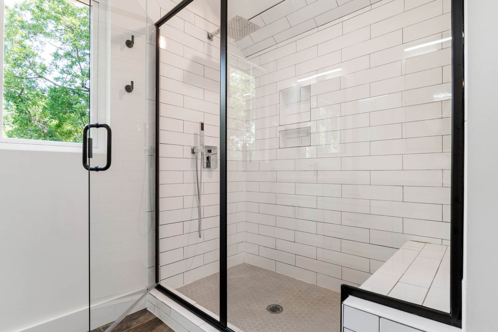 Walk-in shower with a black-framed glass door, white subway tile and a tiled bench