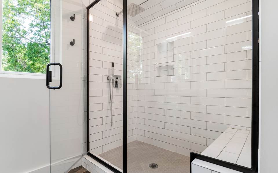 White subway tile walk-in shower with a black-framed glass door, a tiled bench and a window
