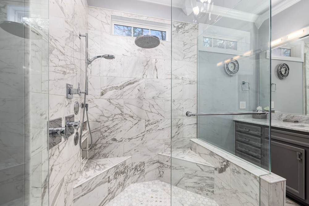 Marble-look tile walk-in shower with two corner benches, a rain head, a hand shower on a slide bar and frameless glass panels
