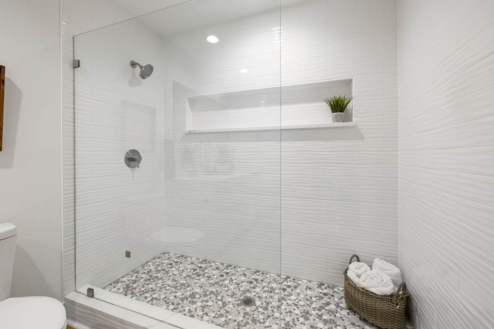 Walk-in shower with one fixed glass panel, white wave tile, a long niche and a pebble mosaic floor