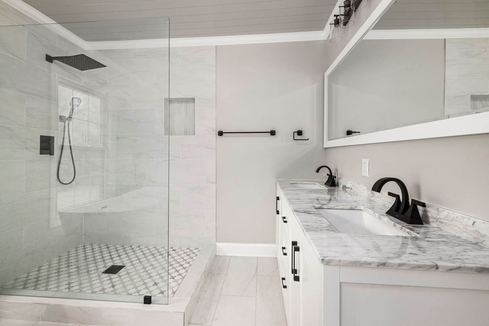 Tiled walk-in shower behind a single glass panel, with a niche, a black rain head and a marble-top double vanity