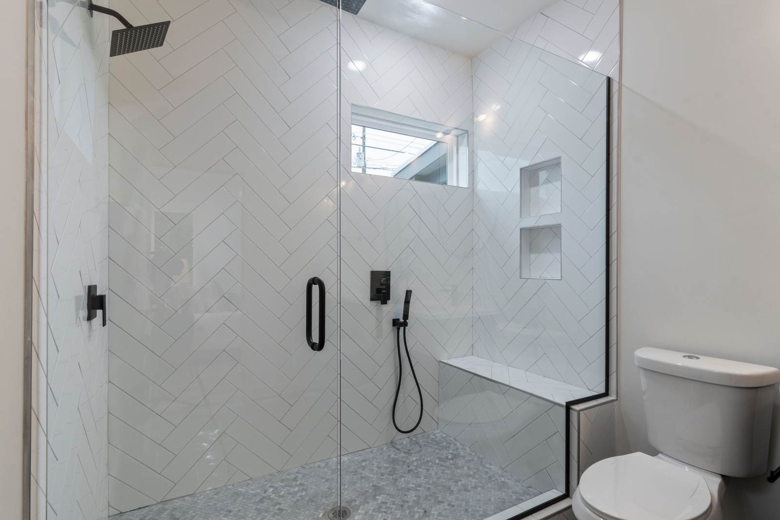 Walk-in shower with white herringbone tile, a built-in bench and a frameless glass door