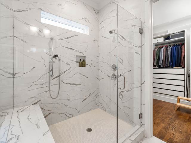 Walk-in shower with marble-look tile, a built-in bench, and a frameless glass panel