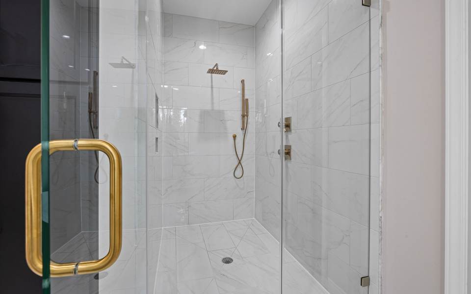 Walk-in shower with large white marble-look tile, a glass door with a brass handle and brass fixtures