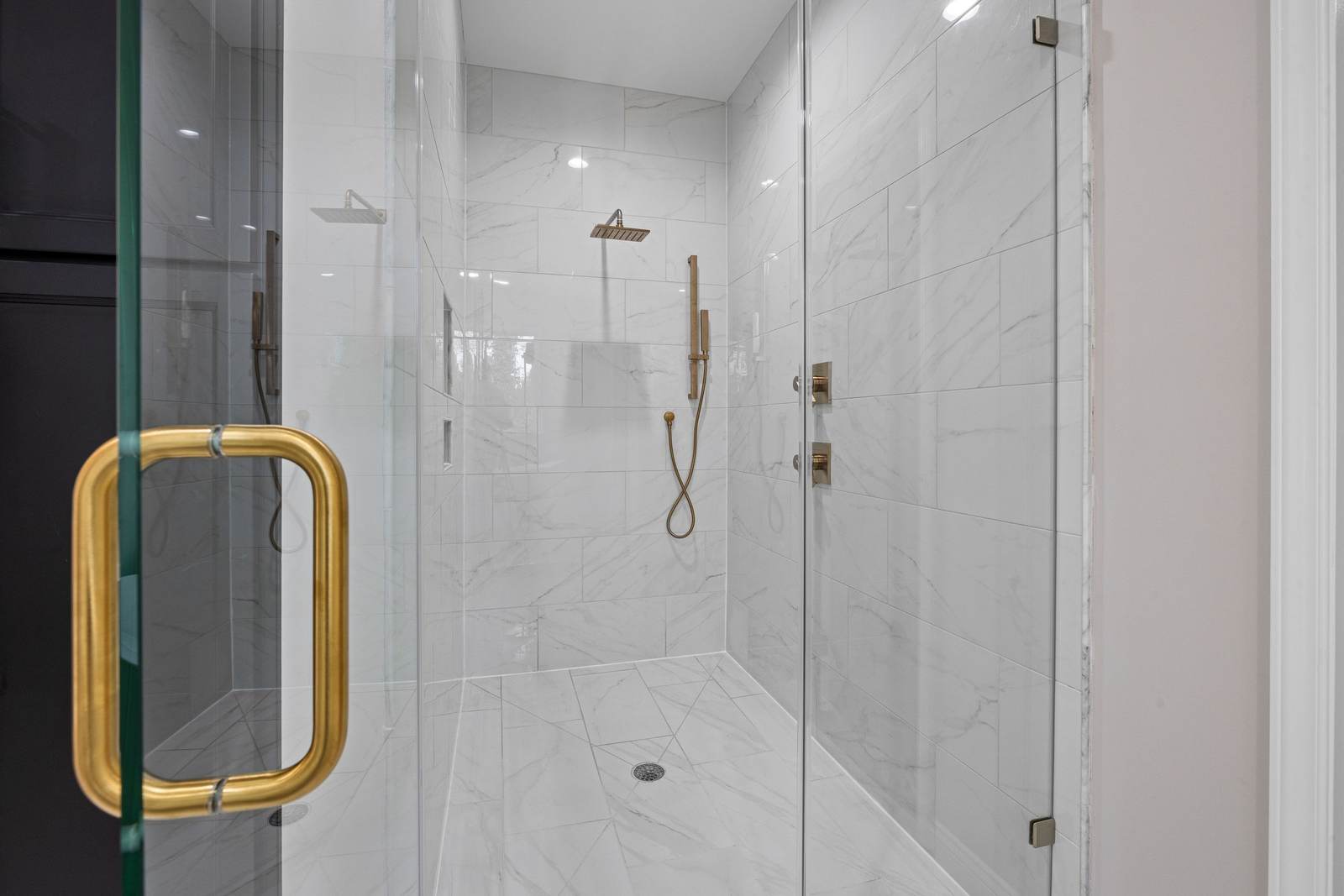 Shower with large-format white tile walls, a frameless glass door and brass fixtures