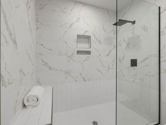 Walk-in shower with marble-look tile, a recessed niche, a low bench, and a fixed glass panel