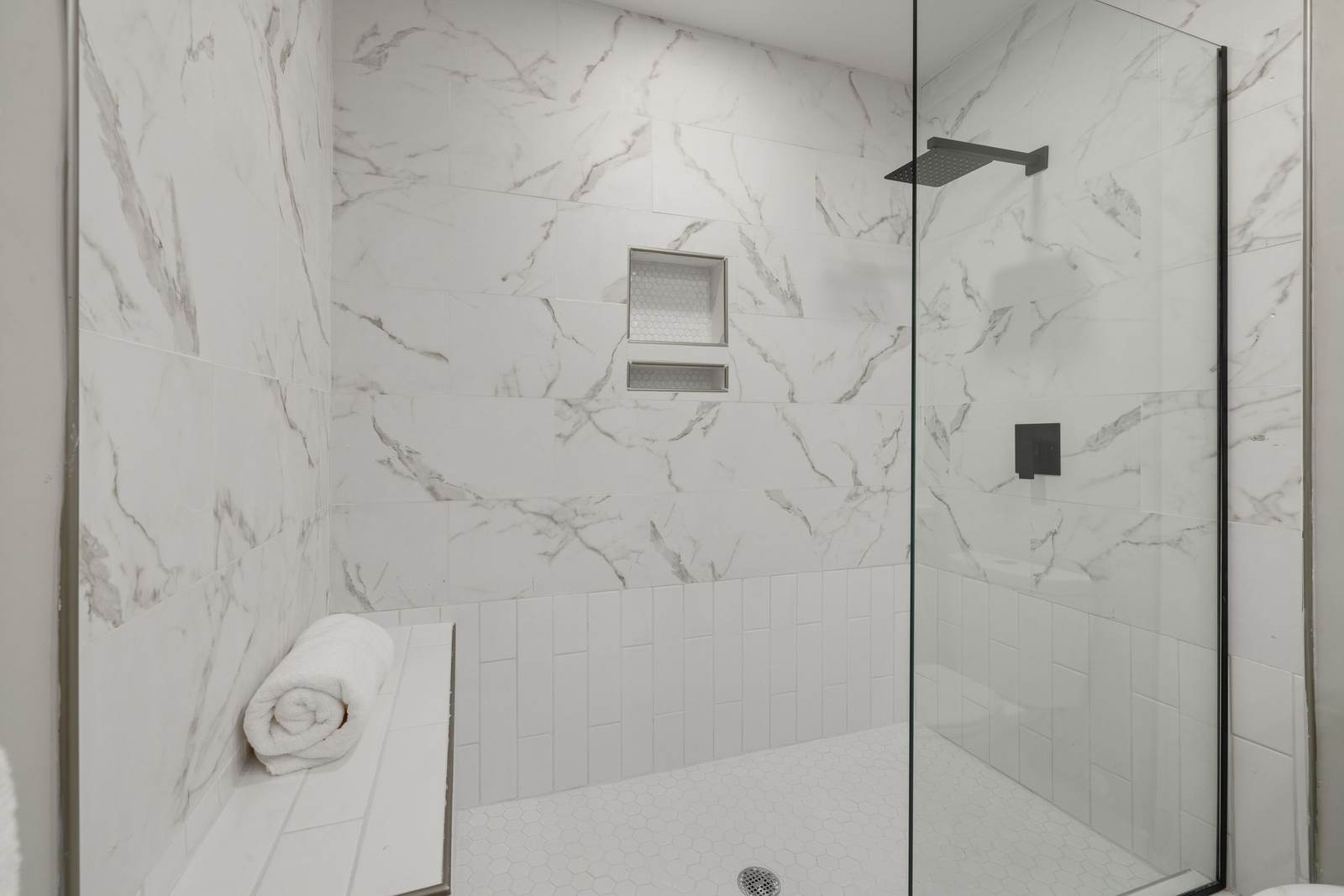 Walk-in shower with a low bench, a recessed niche, and marble-look tile