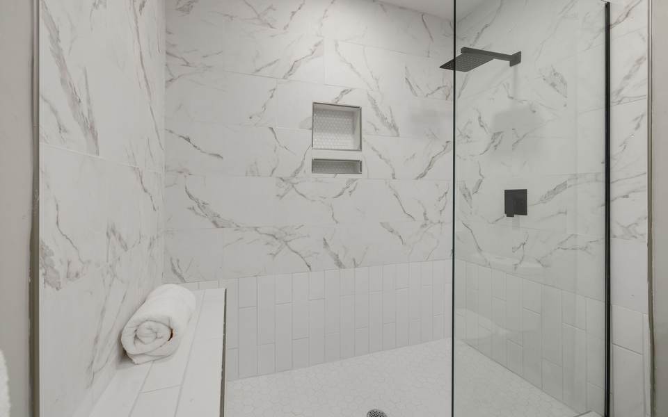 Walk-in shower with marble-look tile, a recessed niche, a low bench and a fixed glass panel