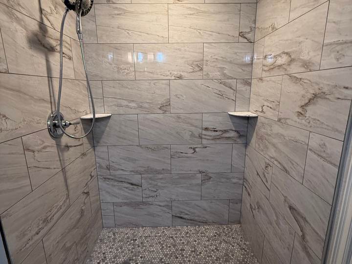 Tiled walk-in shower with marble-look walls and a pebble mosaic floor where a fiberglass tub used to be, in a Bixby home