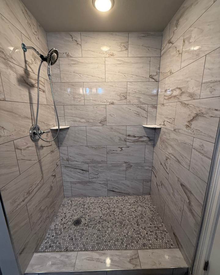 A tiled walk-in shower with marble-look walls and a pebble mosaic floor