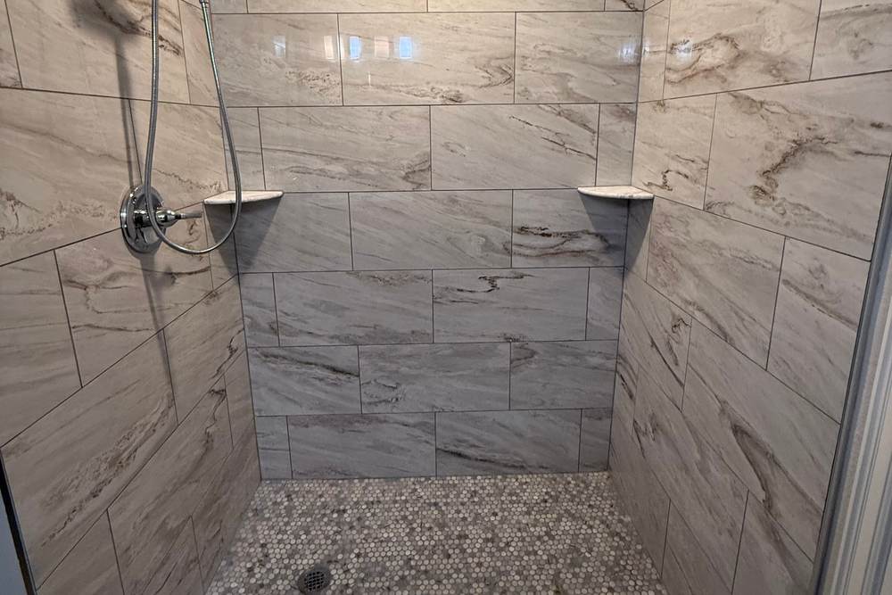 Tiled walk-in shower with marble-look walls, a pebble mosaic floor and a hand shower, where a fiberglass tub and shower combo used to be, in a Bixby home