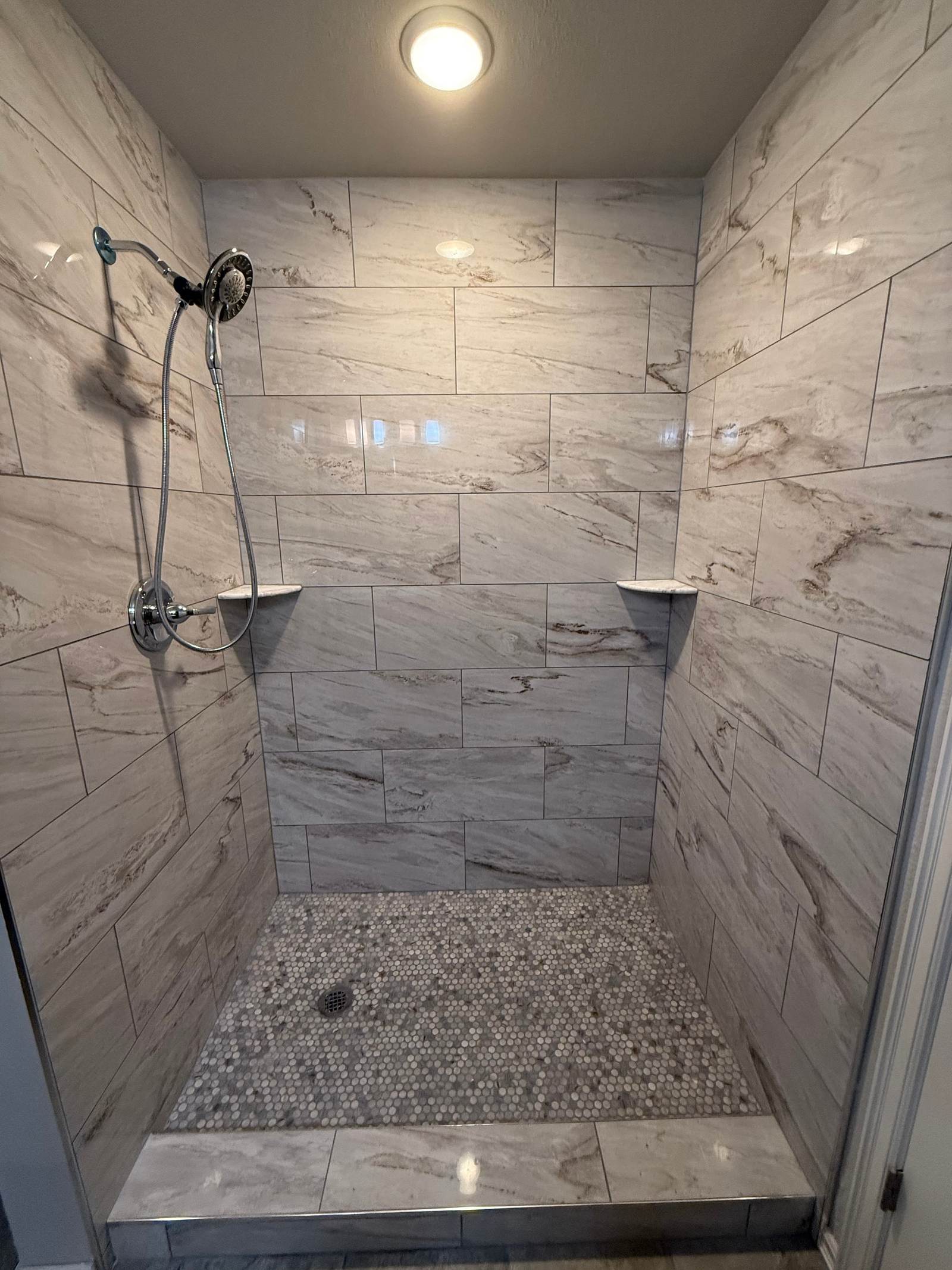 Tiled walk-in shower with marble-look walls, a pebble mosaic floor and a hand shower, built where a fiberglass tub and shower stood in a Bixby bathroom