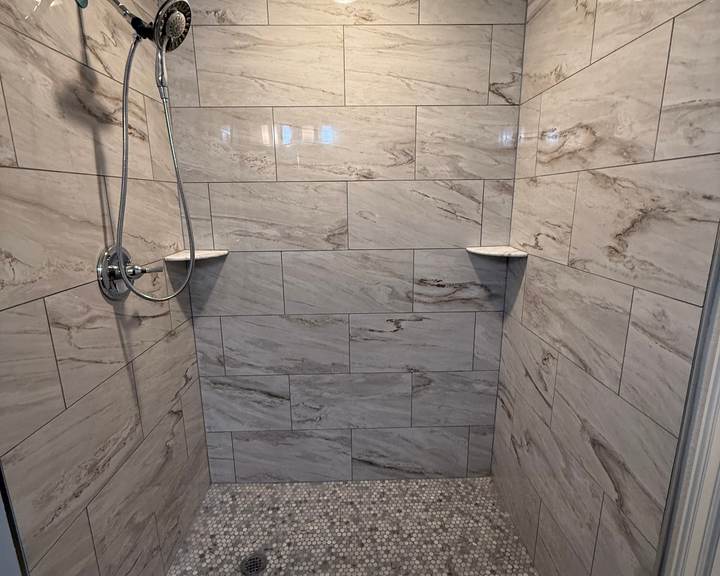 Tiled walk-in shower with marble-look walls and a pebble mosaic floor where a fiberglass tub used to be, in a Bixby home