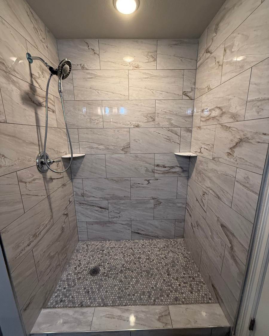 After: a tiled walk-in shower with marble-look walls, a pebble mosaic floor and a hand shower in the same Bixby bathroom