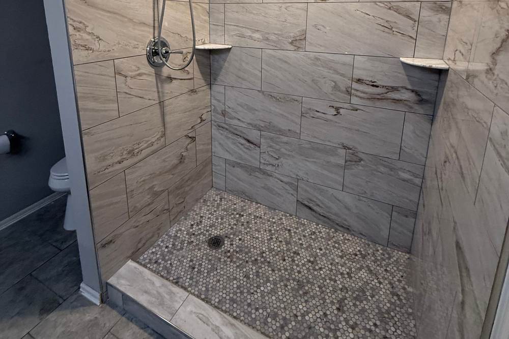 Low tile curb and pebble floor at the entry of a walk-in shower we built in a Bixby home