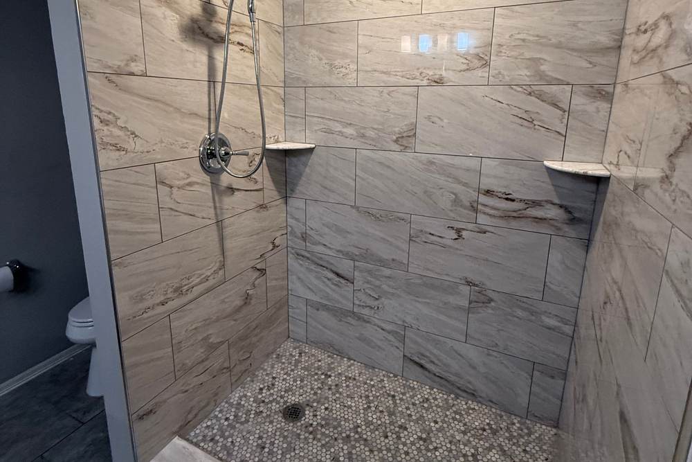 Tiled walk-in shower with a low curb and a pebble floor, built in the space of a fiberglass tub in a Bixby home