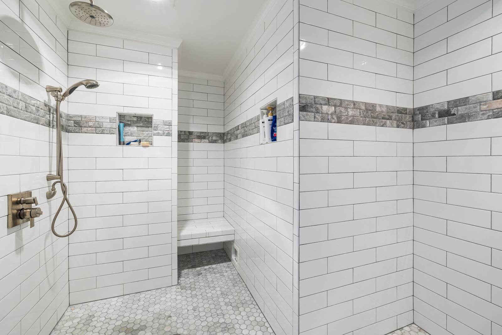 Walk-in shower with a hand shower on a slide bar, a tiled bench and white subway tile