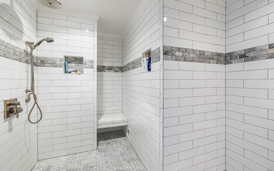 White subway tile walk-in shower with a tiled bench, a niche and a hand shower on a slide bar