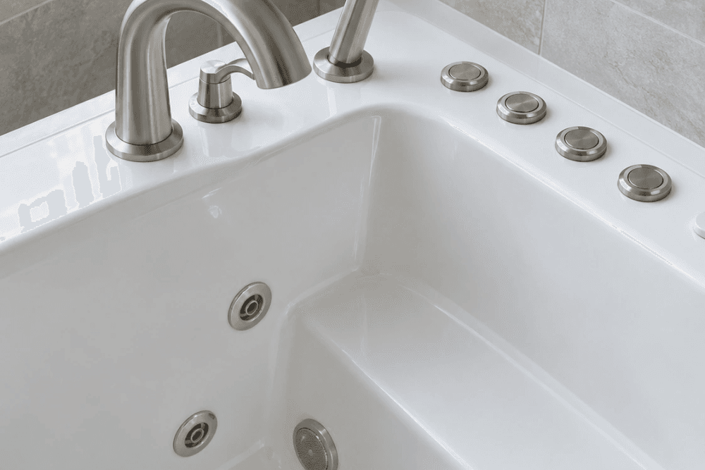 Walk-in tub rim with a brushed nickel faucet, a hand shower and a row of control buttons, above jets in the tub wall