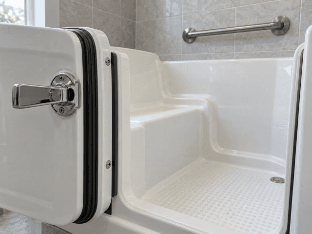 Close-up of a walk-in tub door with its watertight seal and latch handle, the built-in seat and a textured non-slip floor