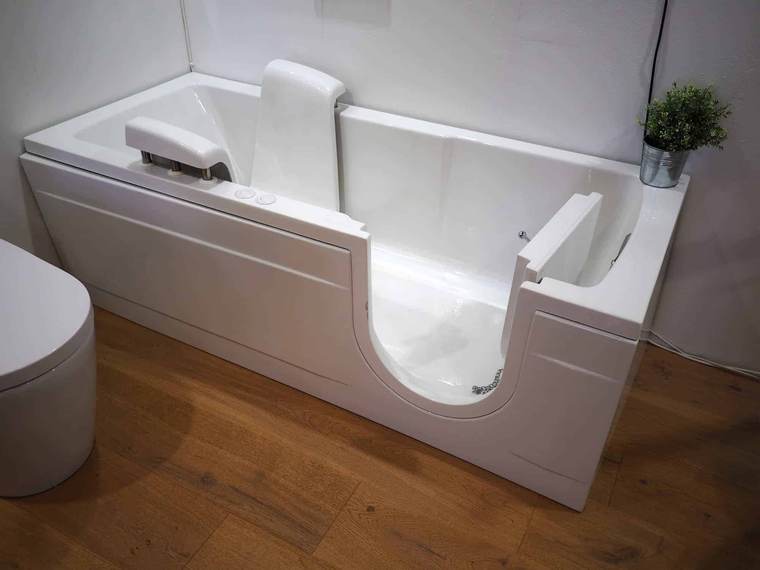Walk-in tub with an open door and built-in seat in a bathroom with wood flooring