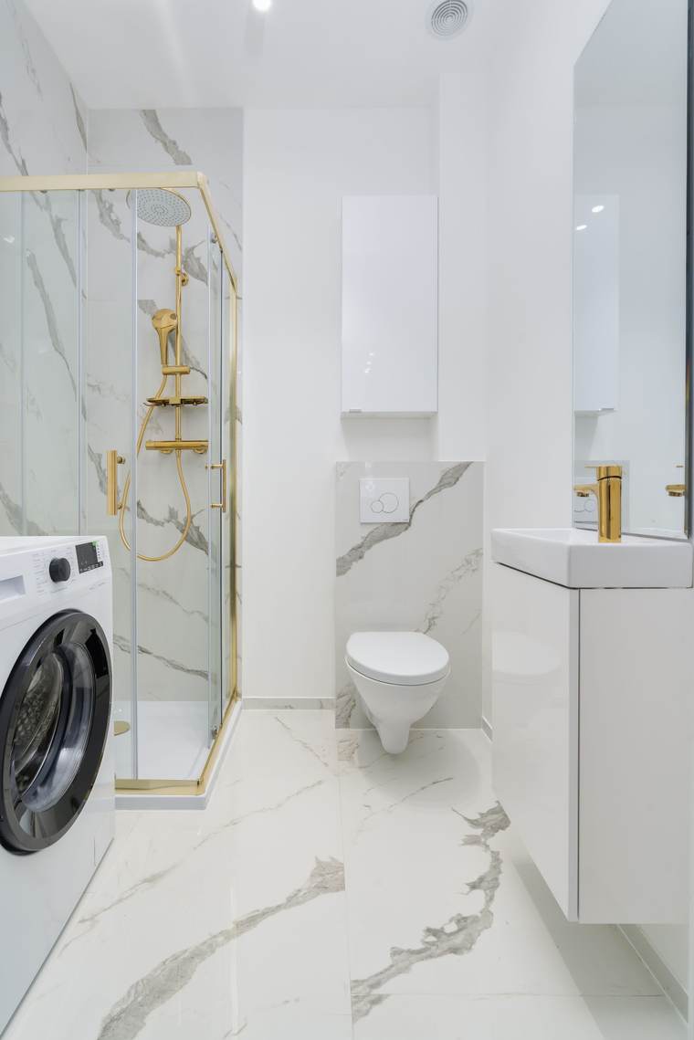 Wall-hung toilet in a marble-look bathroom with gold shower fittings