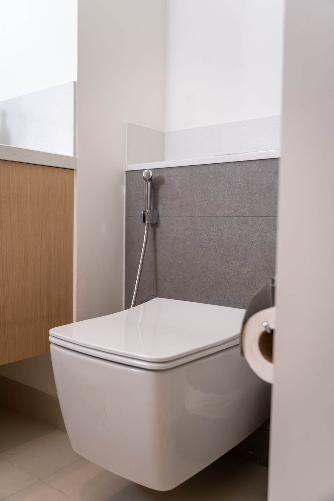 Wall-hung toilet below a chrome in-wall flush plate on gray stone-look tile